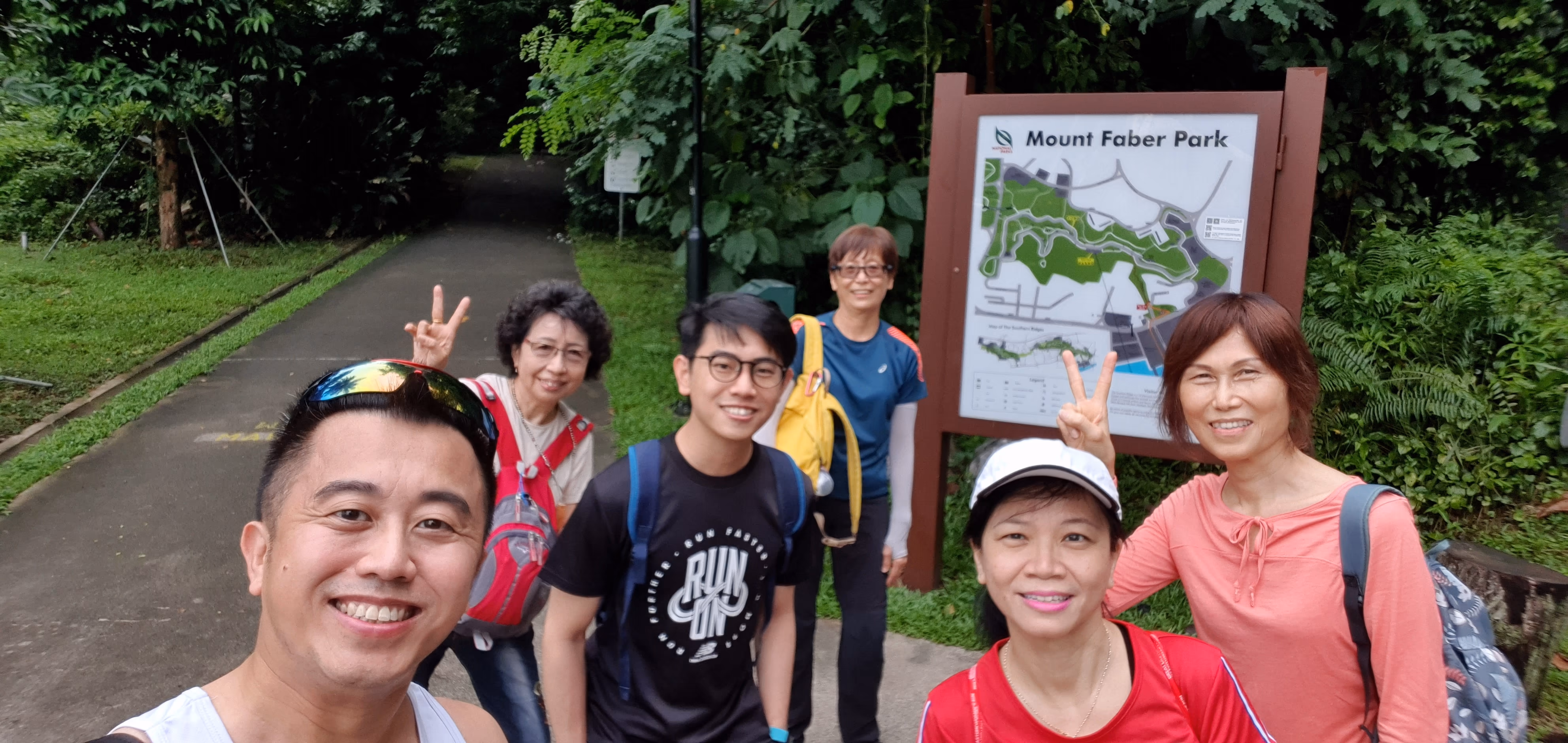 Five smiling people pose for a selfie in front of a Mount Faber Park map sign surrounded by green trees.